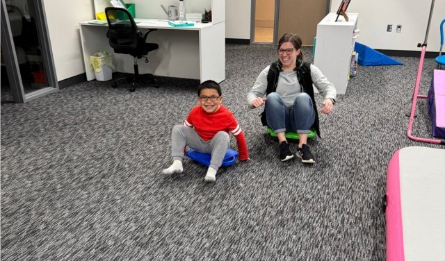 Therapist and child using a scooter for therapy to create movement and fun